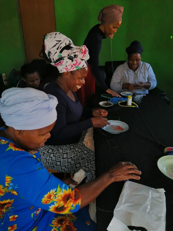 Women in kenya sitting around a table and making beaded jewellery