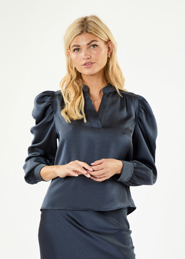 blonde woman wearing the silky blue blouse Neo Noir Rosslyn Sateen Blouse Midnight Blue with puff sleeves and a mandarin collar